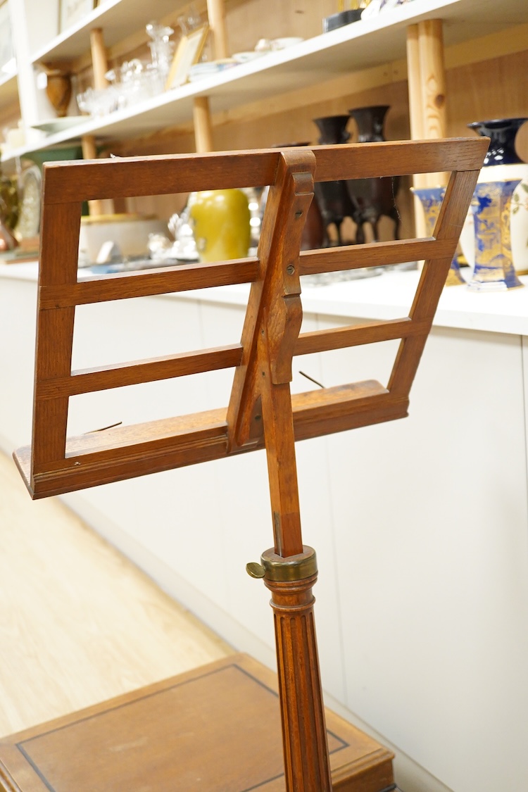 A set of three early 20th century oak music stands, all with fluted pedestal supports and tripod legs with brass feet, adjustable height music desks, maximum overall height when extended 137cm, the angle of the desks is